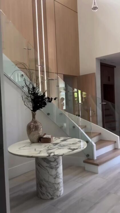 راه پله منحنی مدرن با هندریل شیشه ای، دیوارهای نورپردازی شده و طراحی مینیمال لوکس